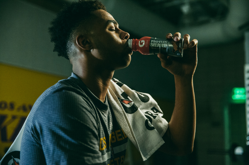 G L Askew II's image for Gatorade of a man drinking a Gatorade Protein Shake. The man is in profile is a dark room and has a Gatorade branded towel over his left shoulder.